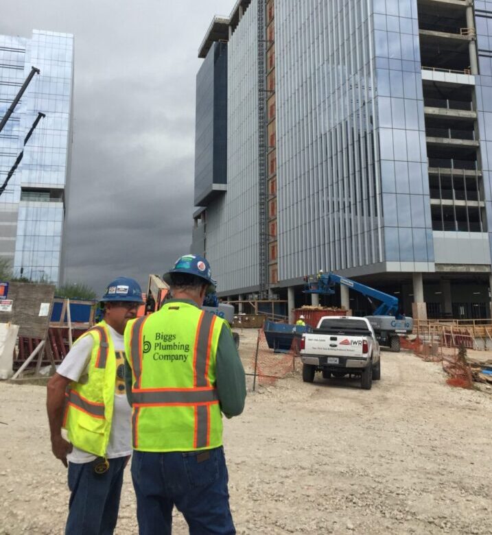 Two workers in bright yellow vests building under construction in the background